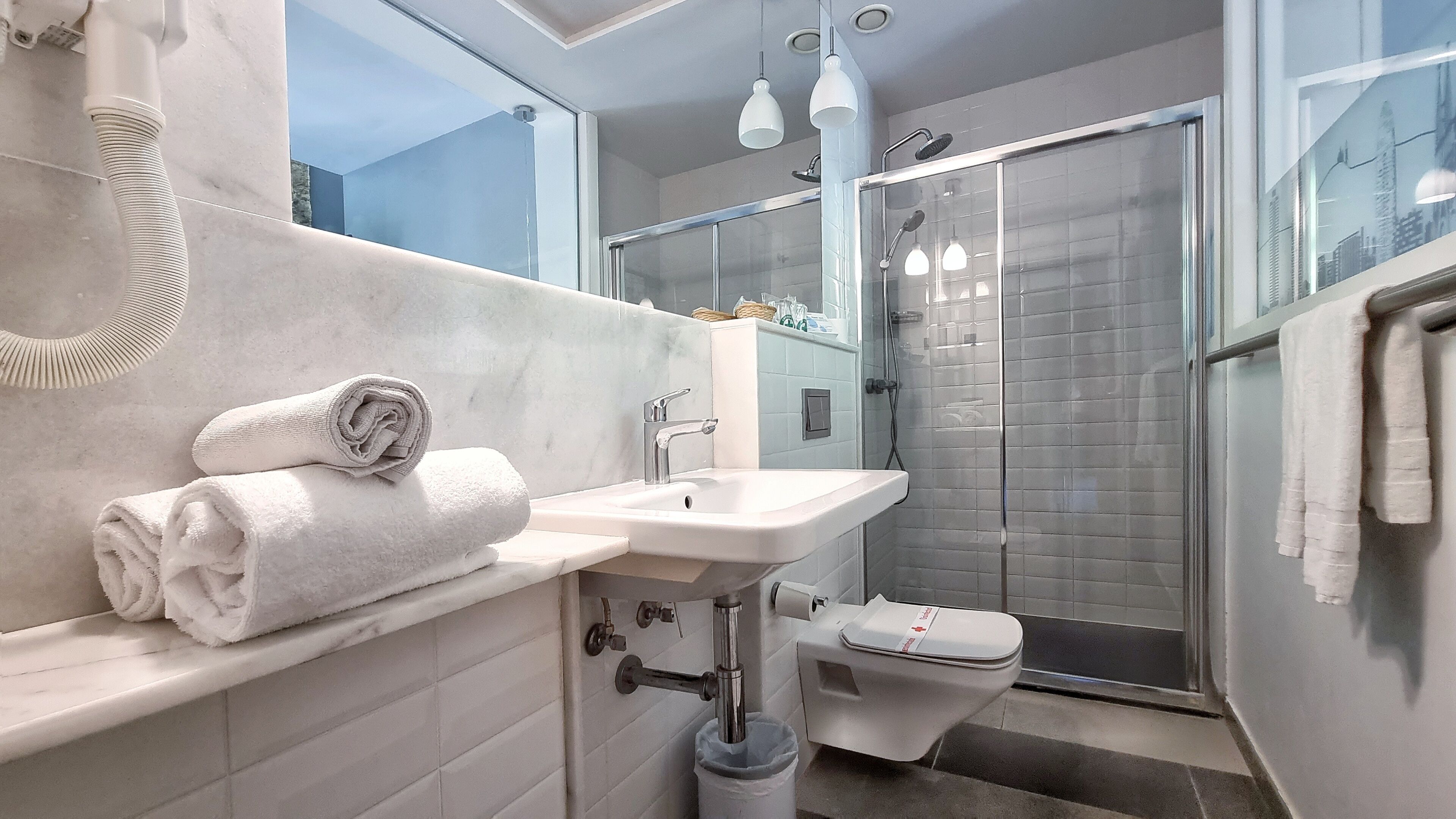 Un baño moderno con un lavamanos blanco, inodoro y ducha con mampara de vidrio.