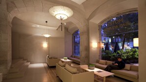 Un moderno vestíbulo de hotel con un arco de piedra, asientos cómodos y vistas de la ciudad a través de amplias ventanas.