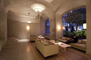 En modern hotellobby med en valvformad entré i sten, bekväma sittplatser och utsikt över stadsbilden genom stora fönster.