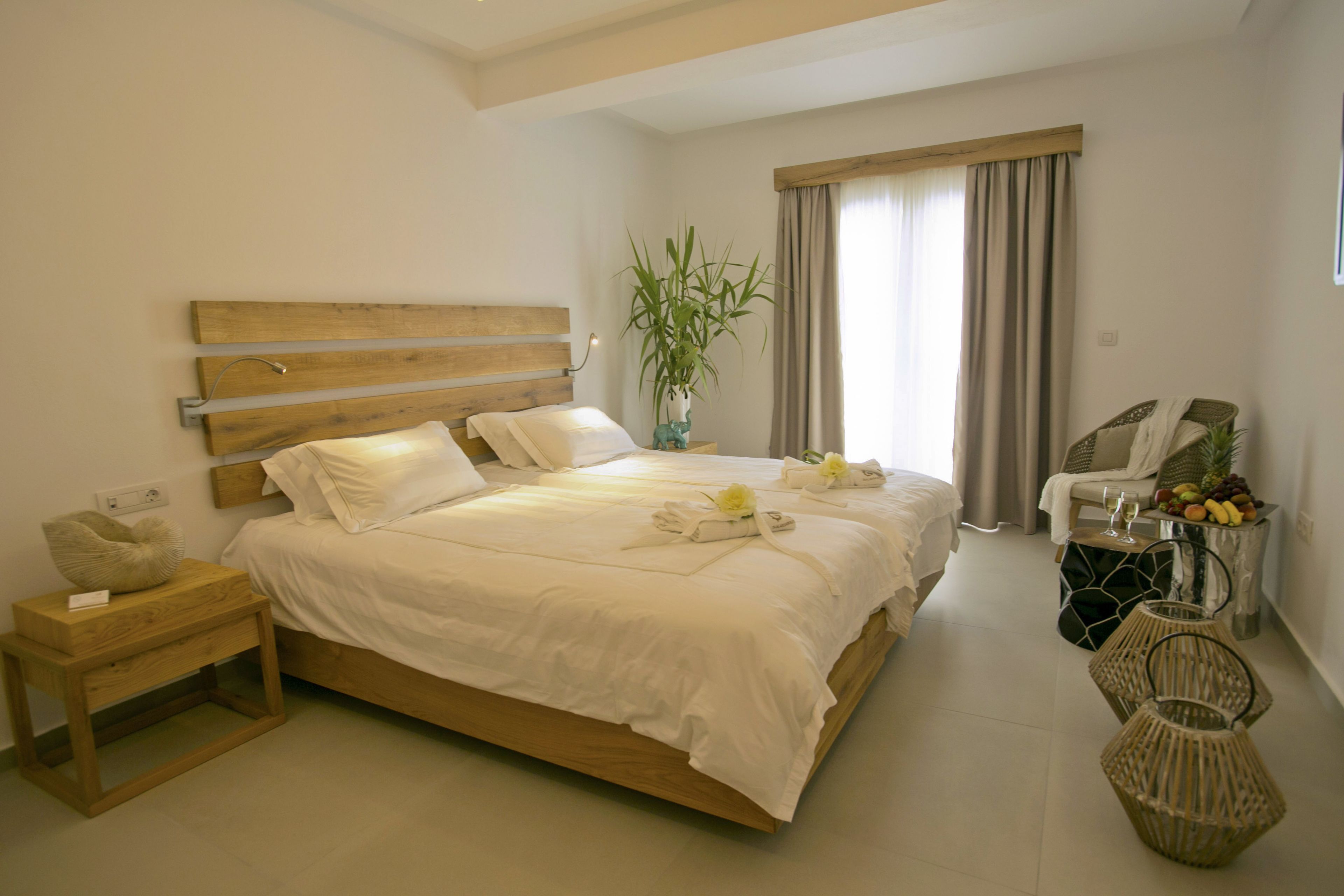 A neatly arranged hotel room with a large bed, a bedside table, a chair, and a small table with fruit and a glass.