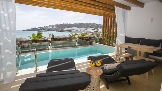 Un área lounge exterior moderna con piscina, sillones y una mesa de madera.