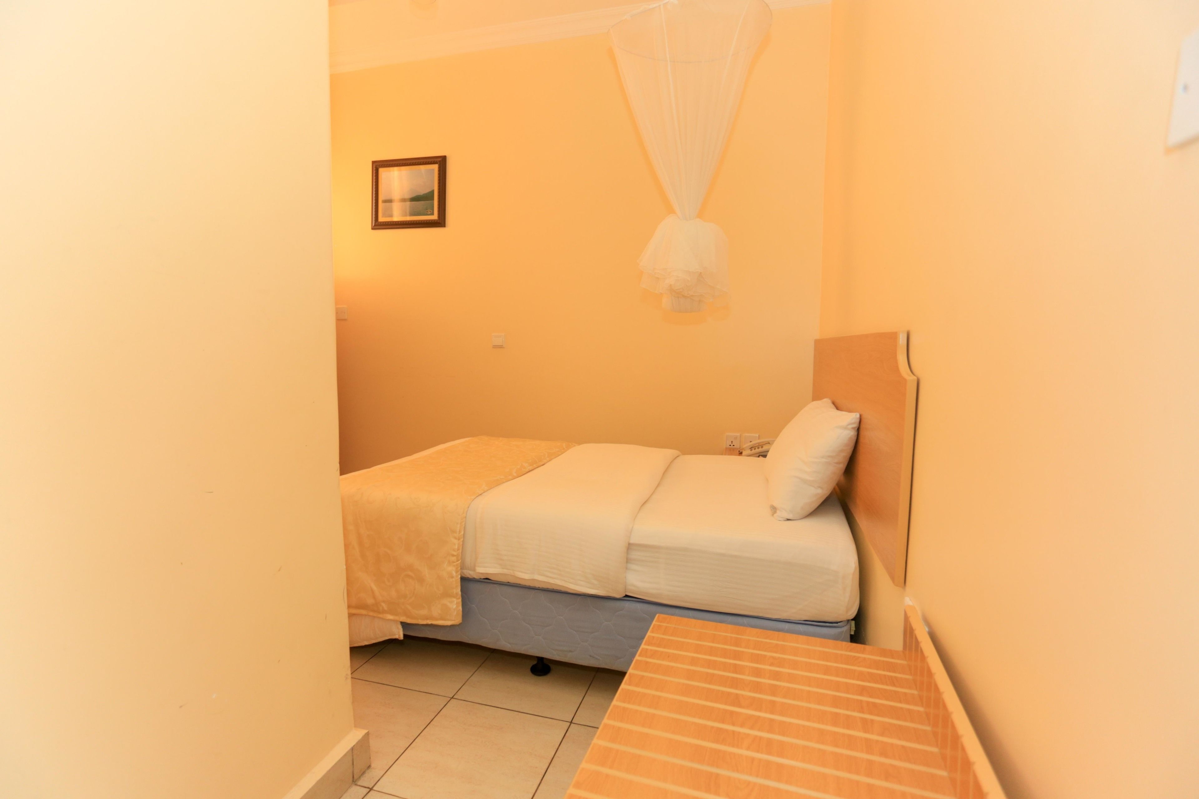 Une petite chambre avec un lit simple, surmontée d’une moustiquaire.