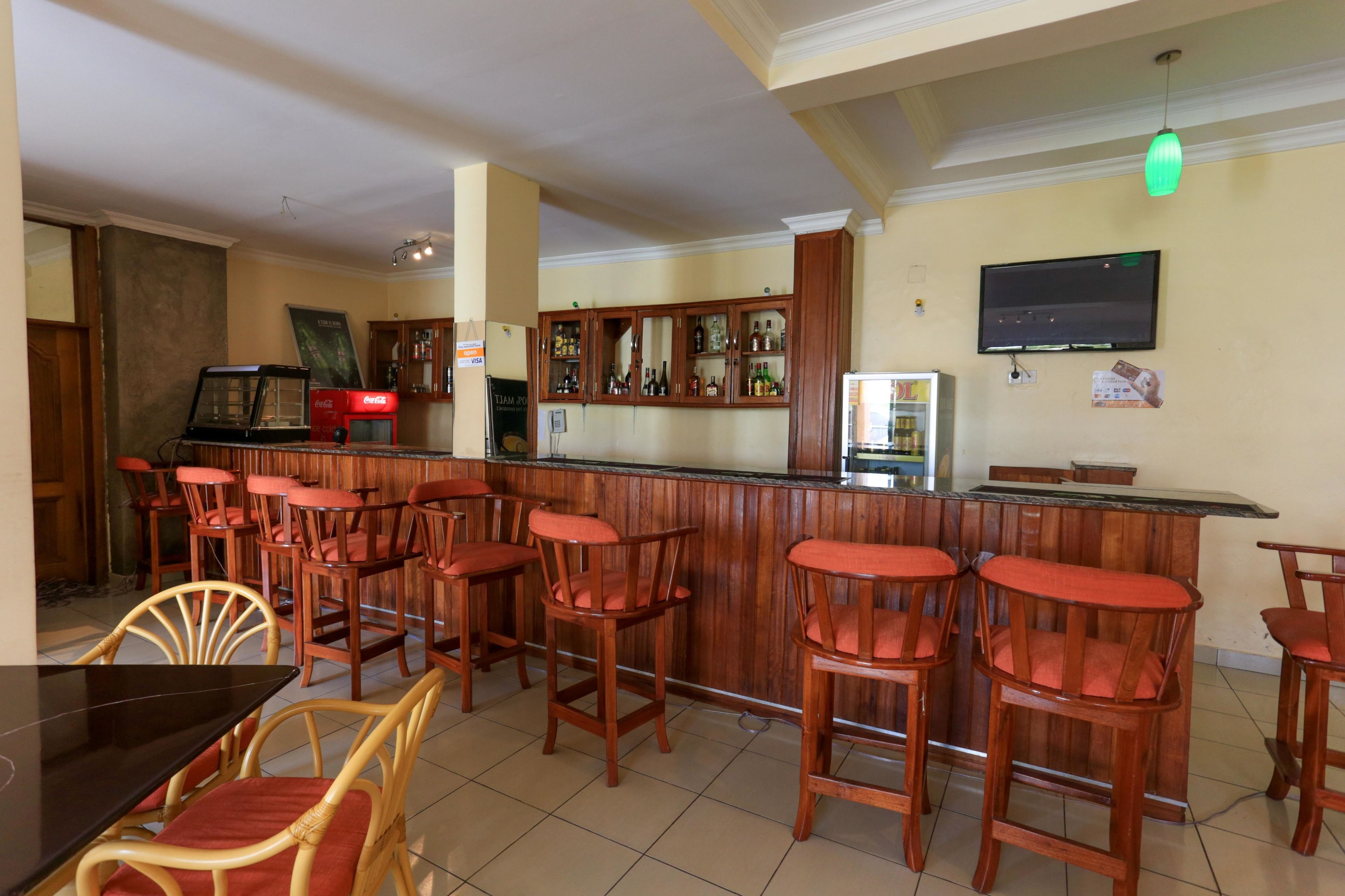 Zona de bar con taburetes de madera y una barra. Hay taburetes con asientos acolchados, una barra y un televisor montado en la pared.