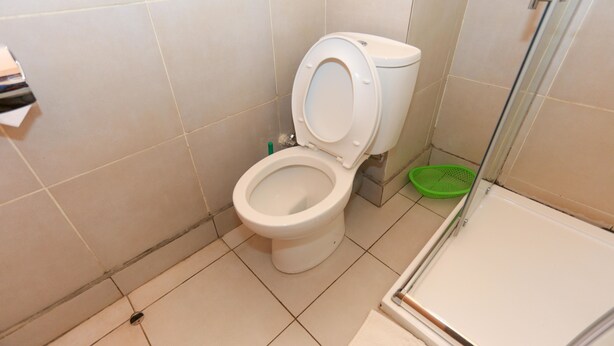 A bathroom with a toilet, a shower, and a green cleaning basket. - Faraja Hotel (Muhoza)