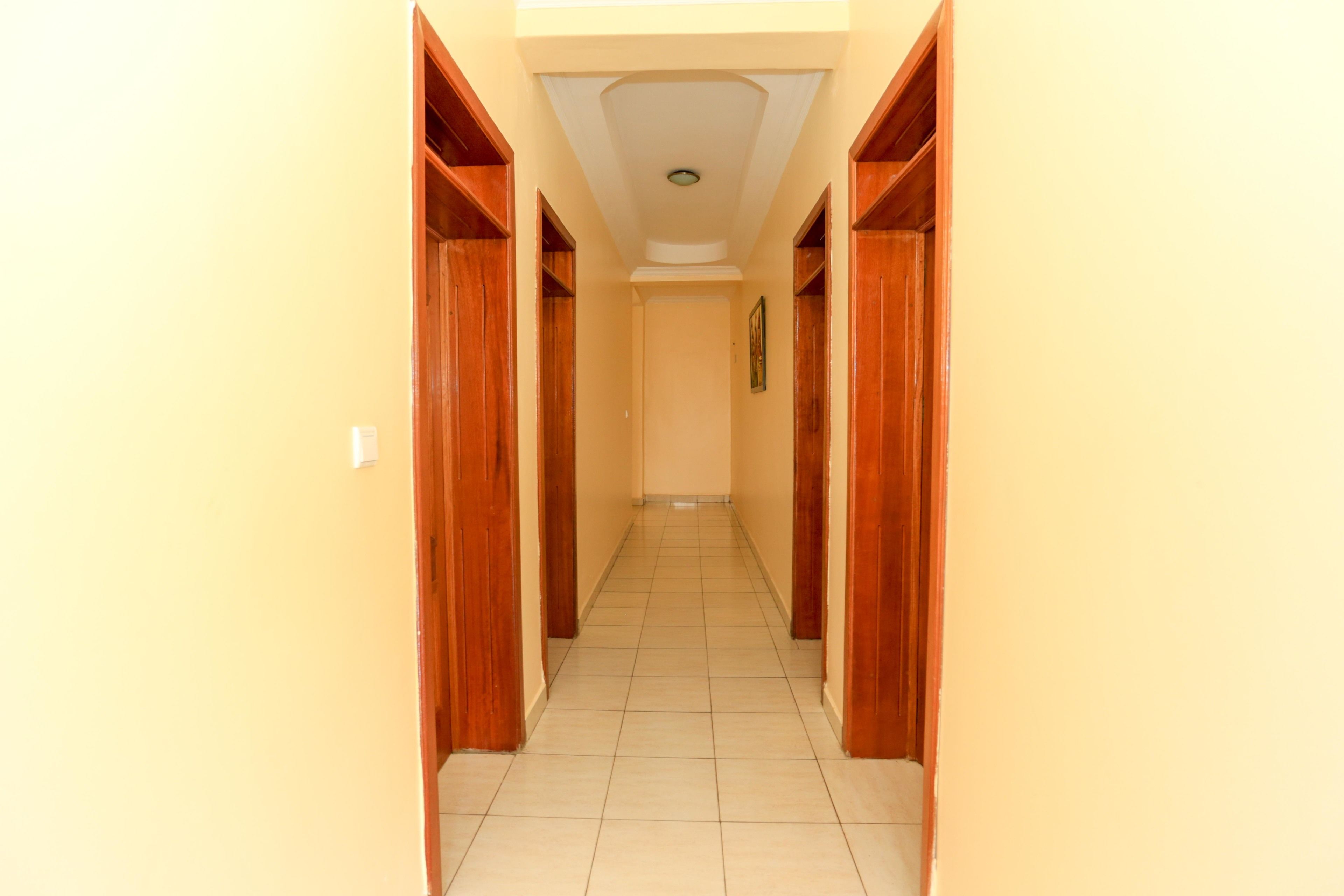 Un pasillo estrecho con puertas de madera a ambos lados y suelo de baldosas.