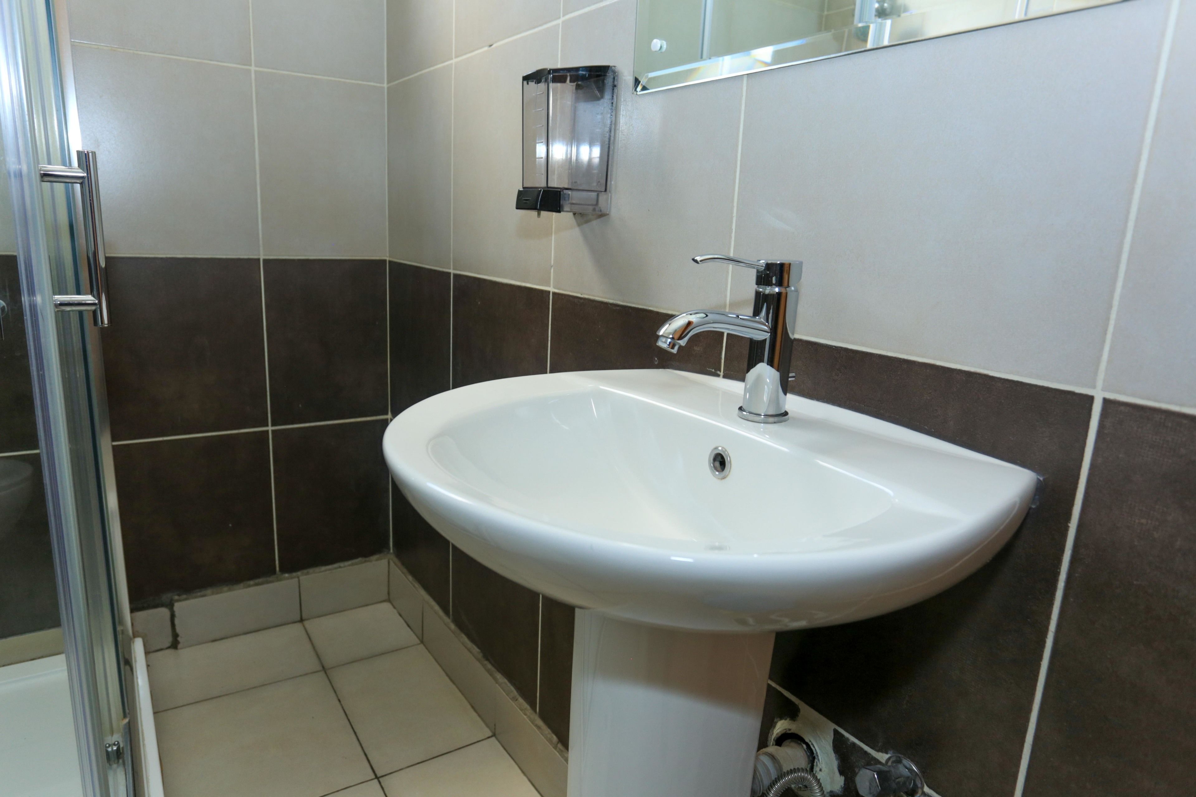 Un baño con lavamanos blanco, espejo y zona de ducha.