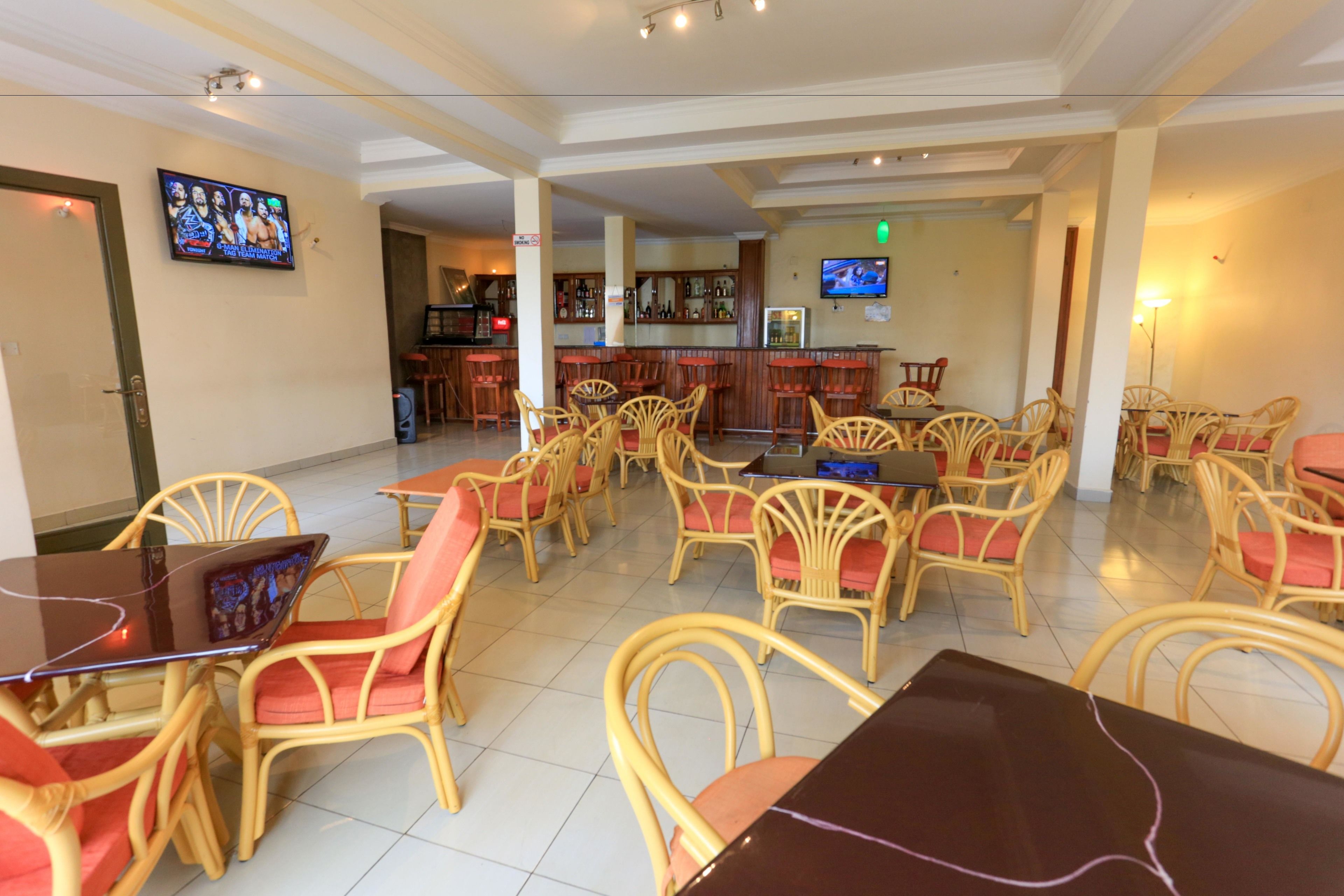 A hotel lobby with wicker chairs, a bar area, and a television on the wall.