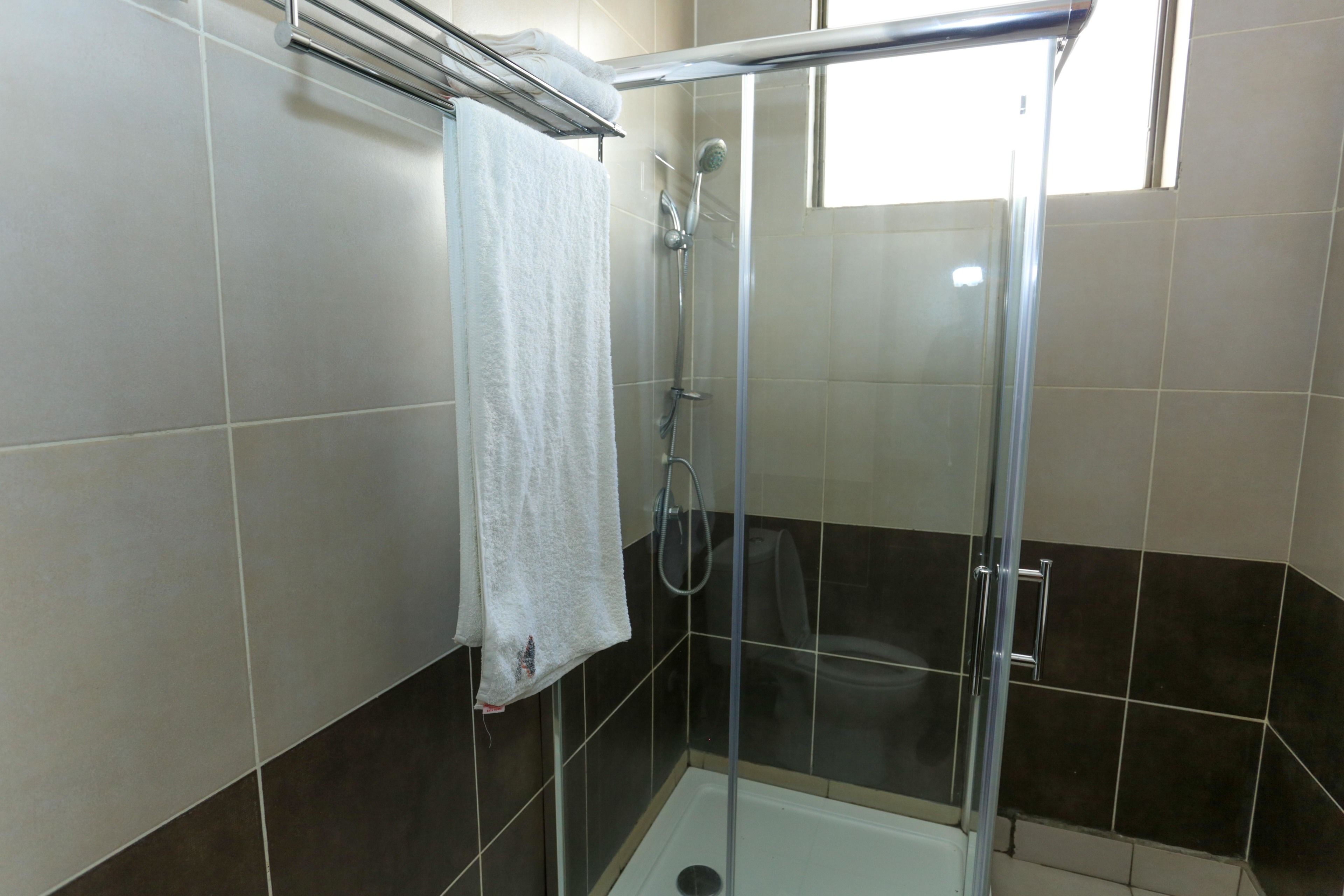 Ducha con paredes de vidrio, una toalla blanca colgada en un perchero, paredes con azulejos y un ventanal que proporciona luz natural.