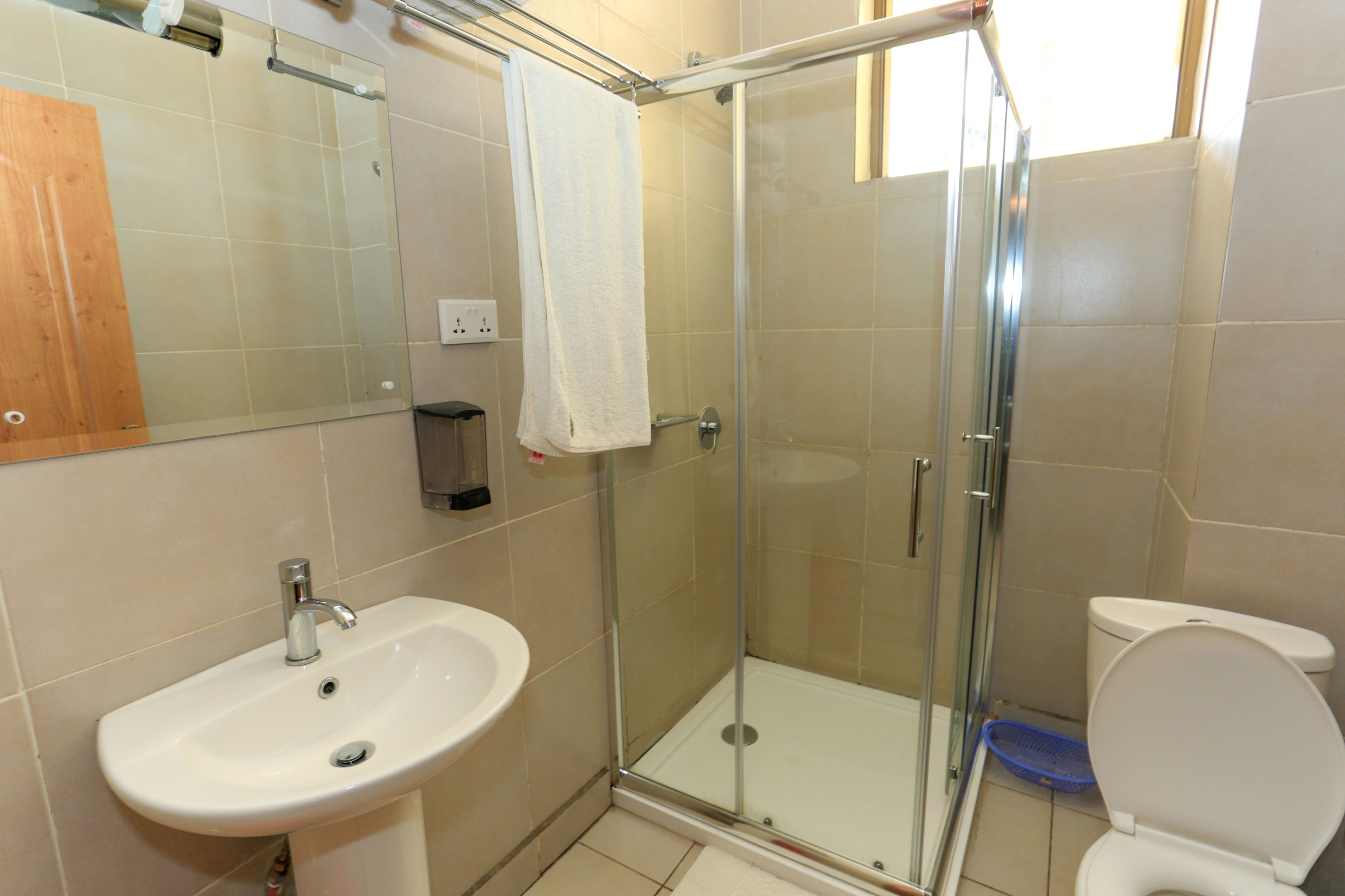 Ein Badezimmer mit einer ein Glaswand trennenden Dusche, einem weißen Waschbecken und einer Toilette.