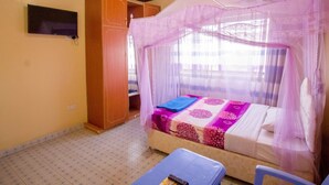 A room with a bed under a mosquito net, a television on the wall, and a wardrobe. - Grande Hotel (Isiolo)