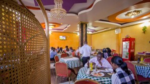 A restaurant with tables covered in checkered tablecloths, a chandelier, and a television screen on the wall. - Grande Hotel (Isiolo)