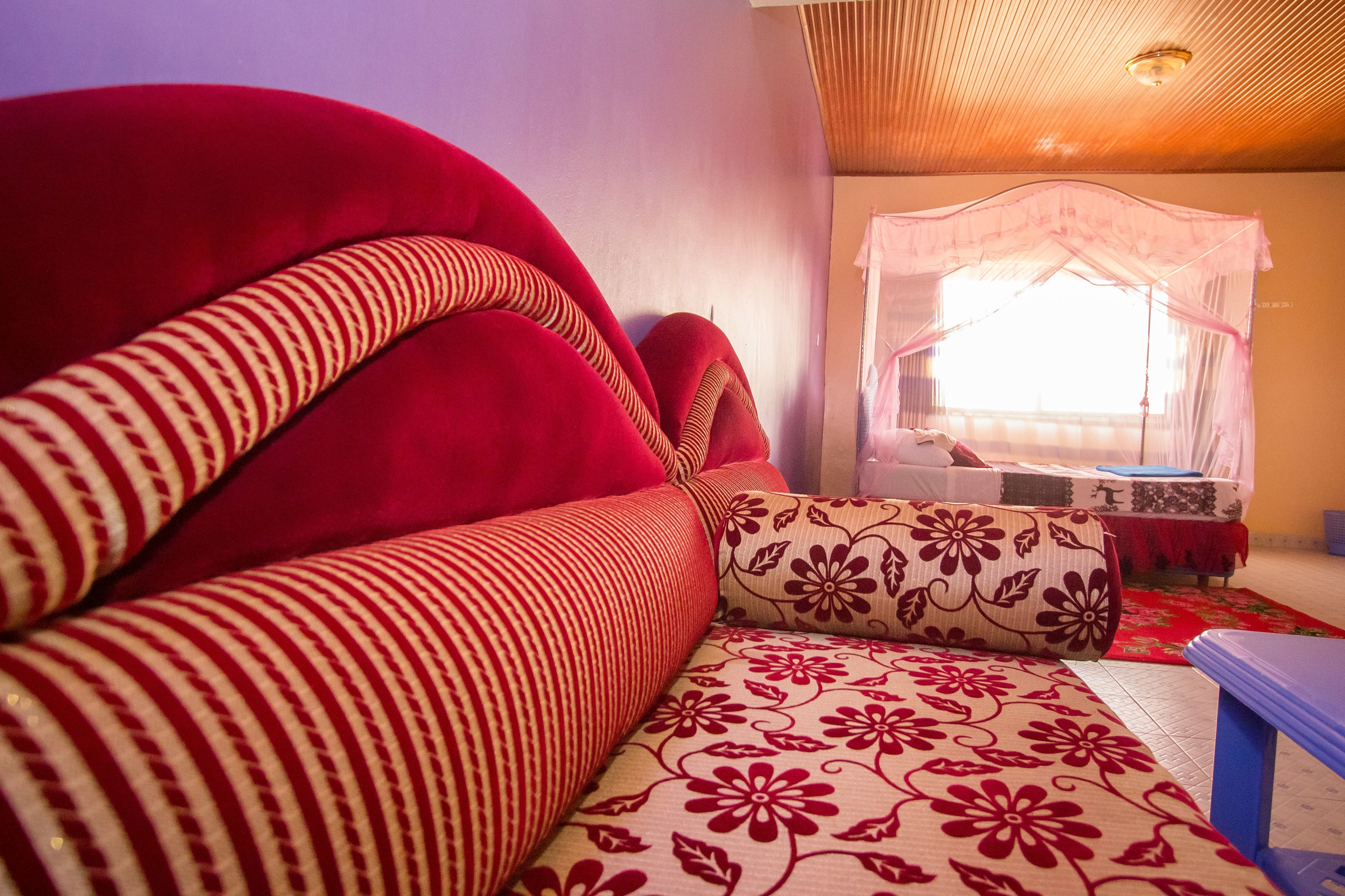 A room with a red sofa, a patterned sofa, a bed with a canopy, and a small table.