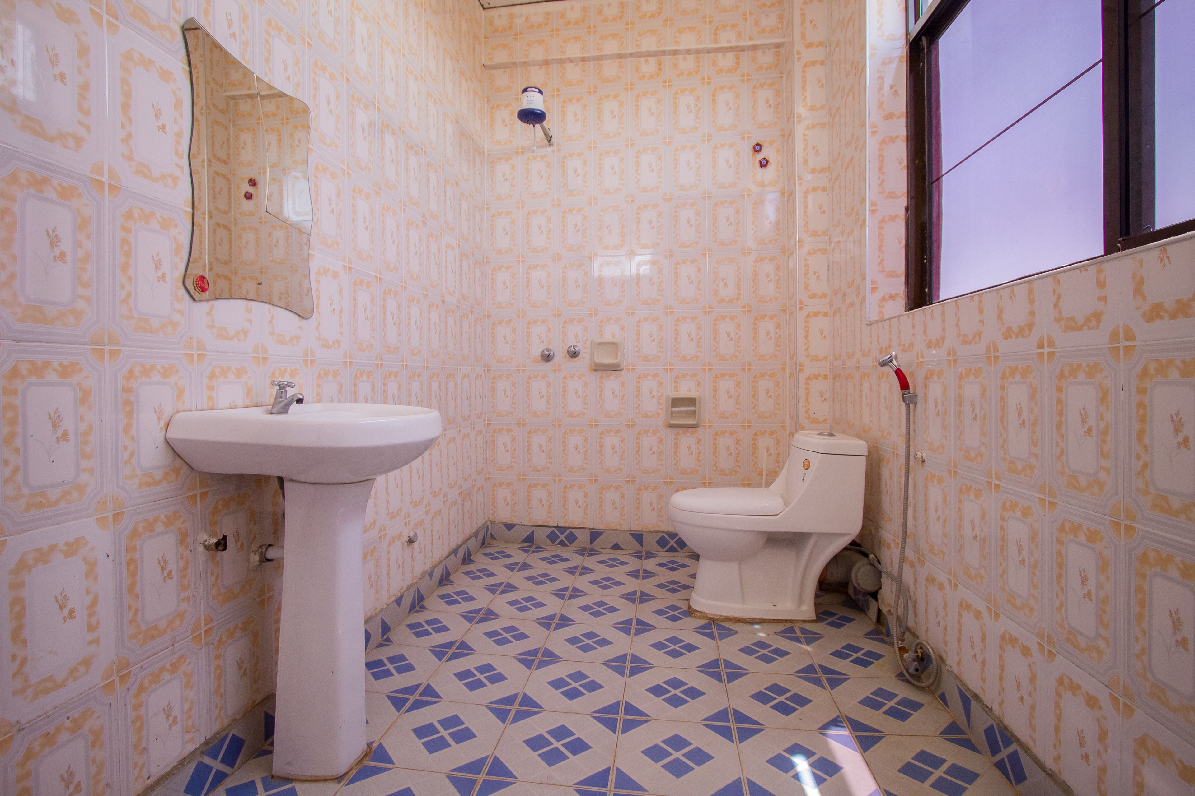 Un baño con lavamanos, inodoro y espejo. Las paredes tienen un diseño de azulejos estampados y el suelo presenta un patrón geométrico de baldosas.