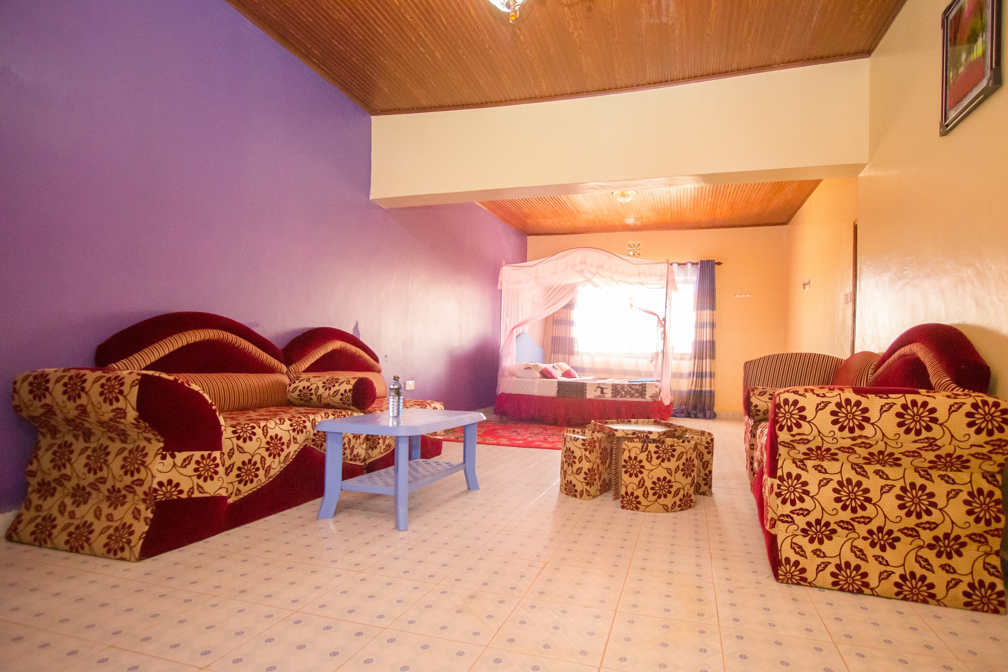 A room with a purple wall, a bed with a canopy, a sofa set, a small table, and a patterned floor.