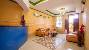 A lobby with a reception desk, seating area, and a decorative vase with flowers. - Grande Hotel (Isiolo)