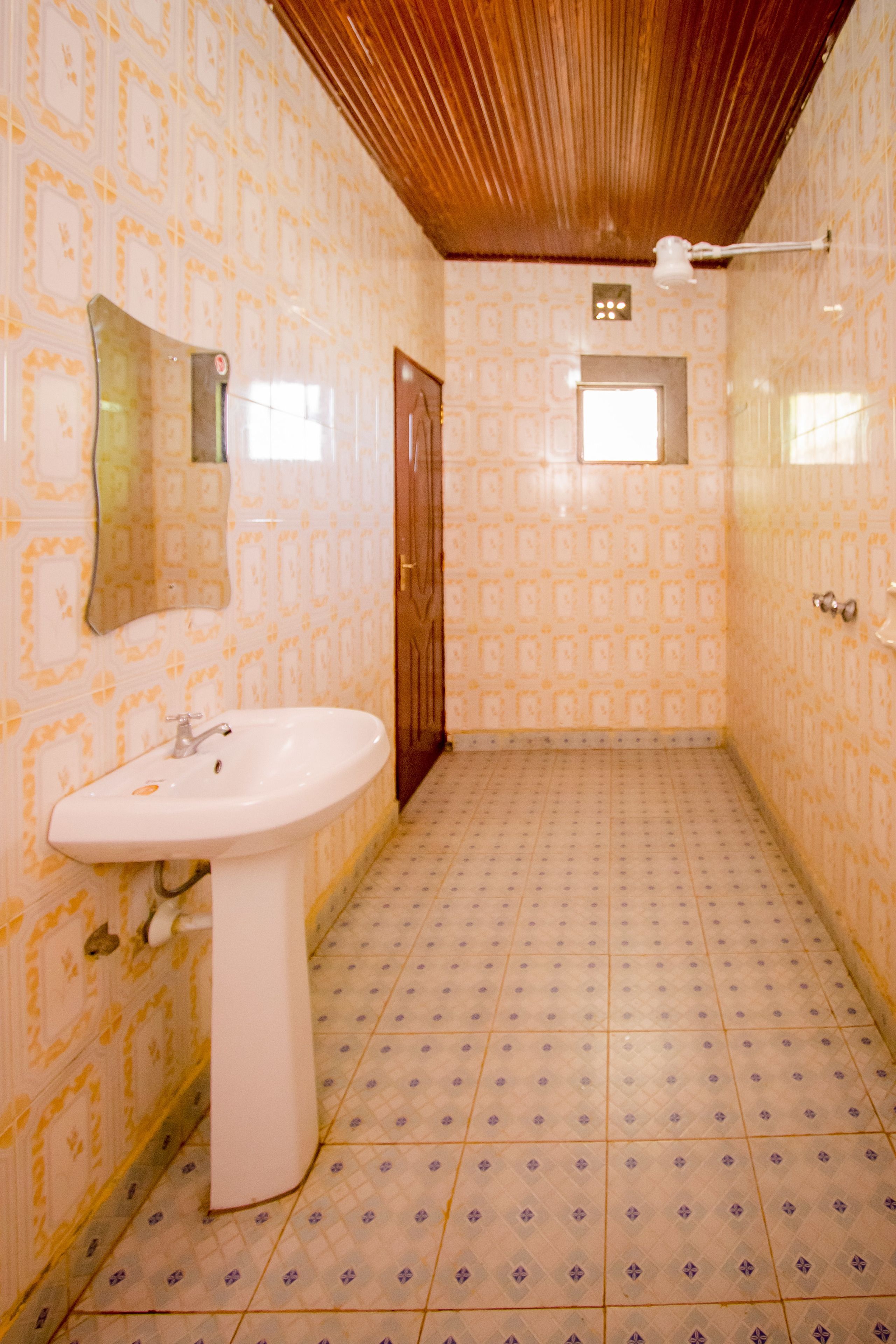 Un baño con papel tapiz estampado, un lavamanos, un espejo y techo de madera.