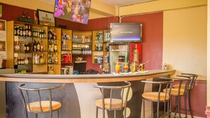 Eine Bar mit einer Theke, Barhocker, Regalen voller Flaschen und einem an der Wand montierten Fernseher.