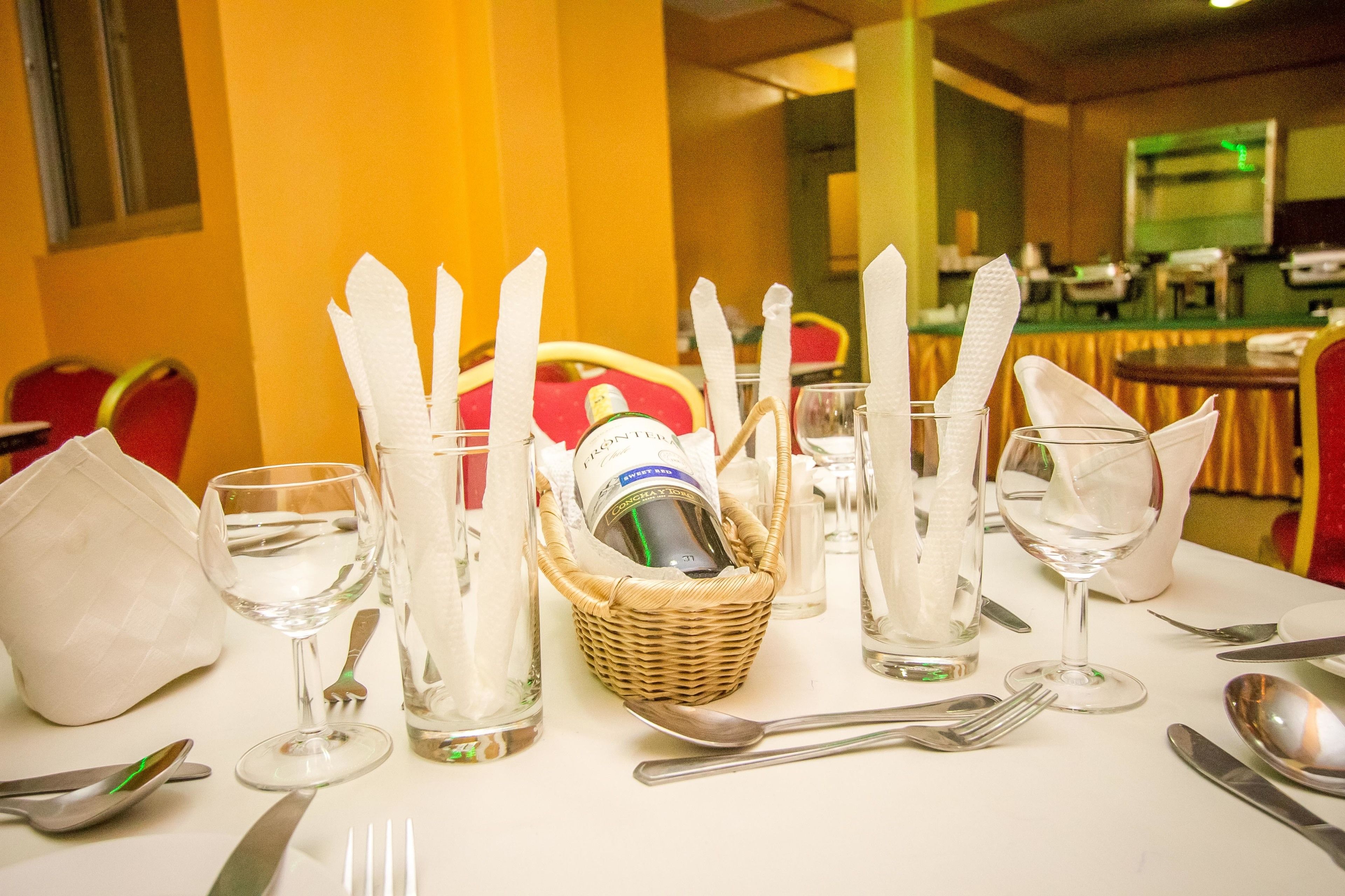A table set with wine glasses, cutlery, and a bottle of liquor in a wicker basket.