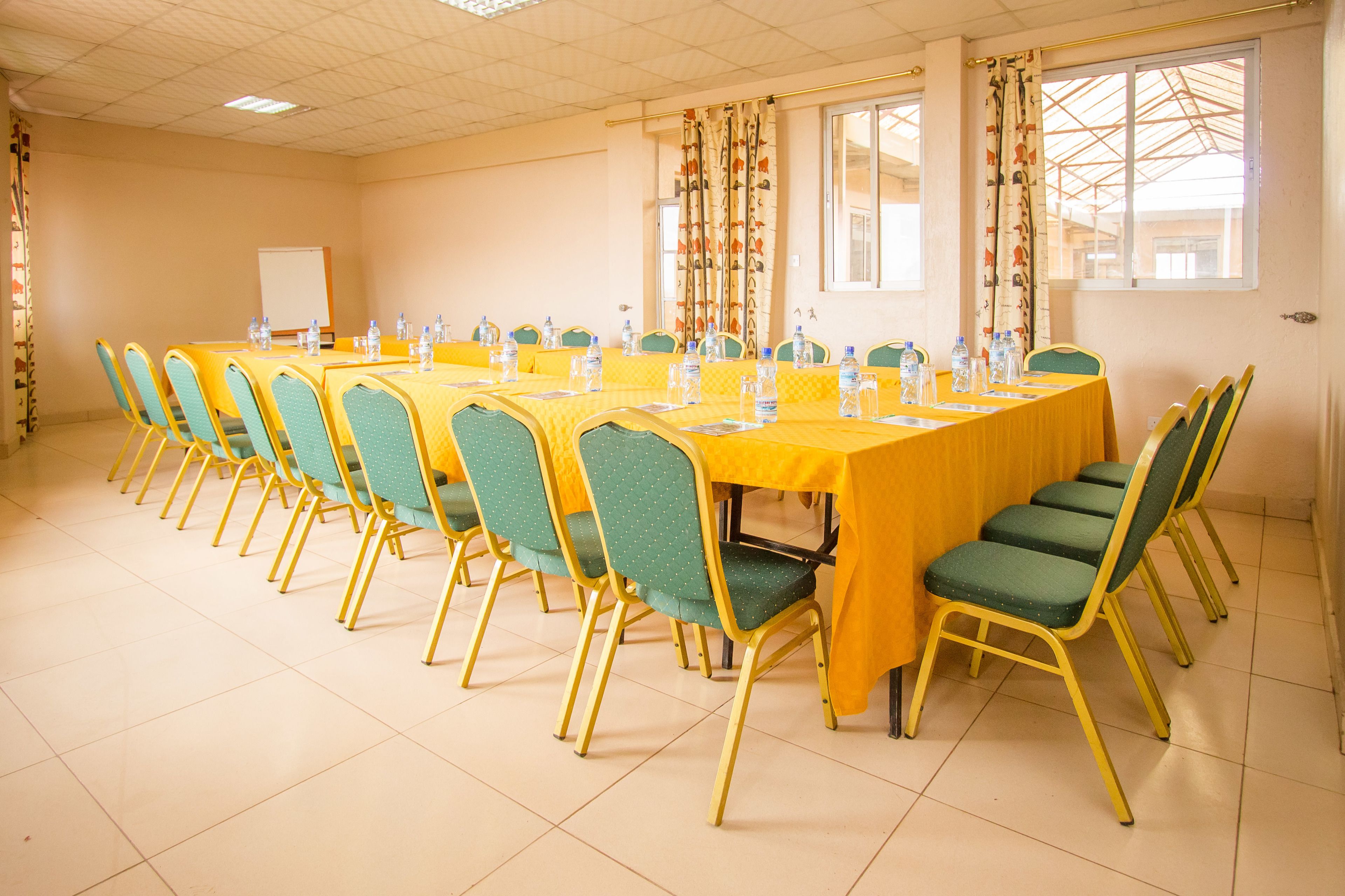 A conference room with multiple tables and chairs, a whiteboard, and windows with curtains.