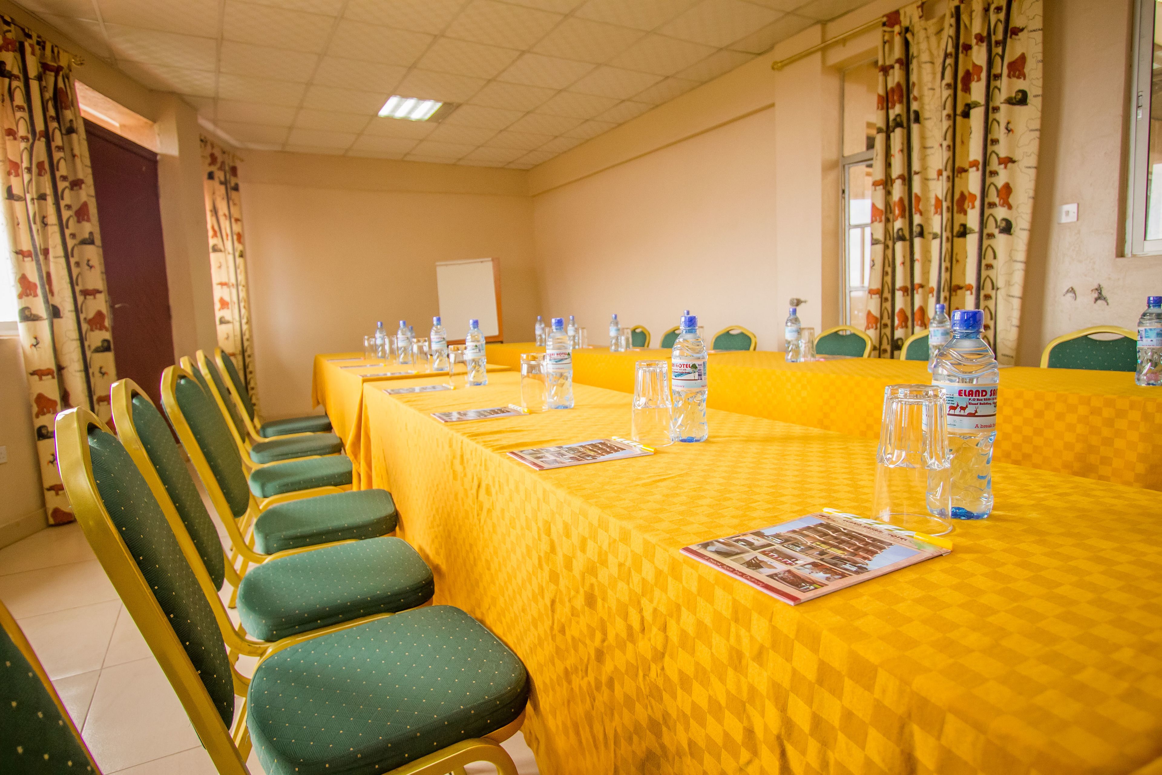 A conference room with a yellow table, green chairs, water bottles, and a whiteboard.