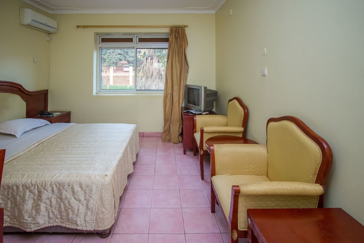 Quarto de hotel com cama, televisão, duas cadeiras e uma mesa pequena.