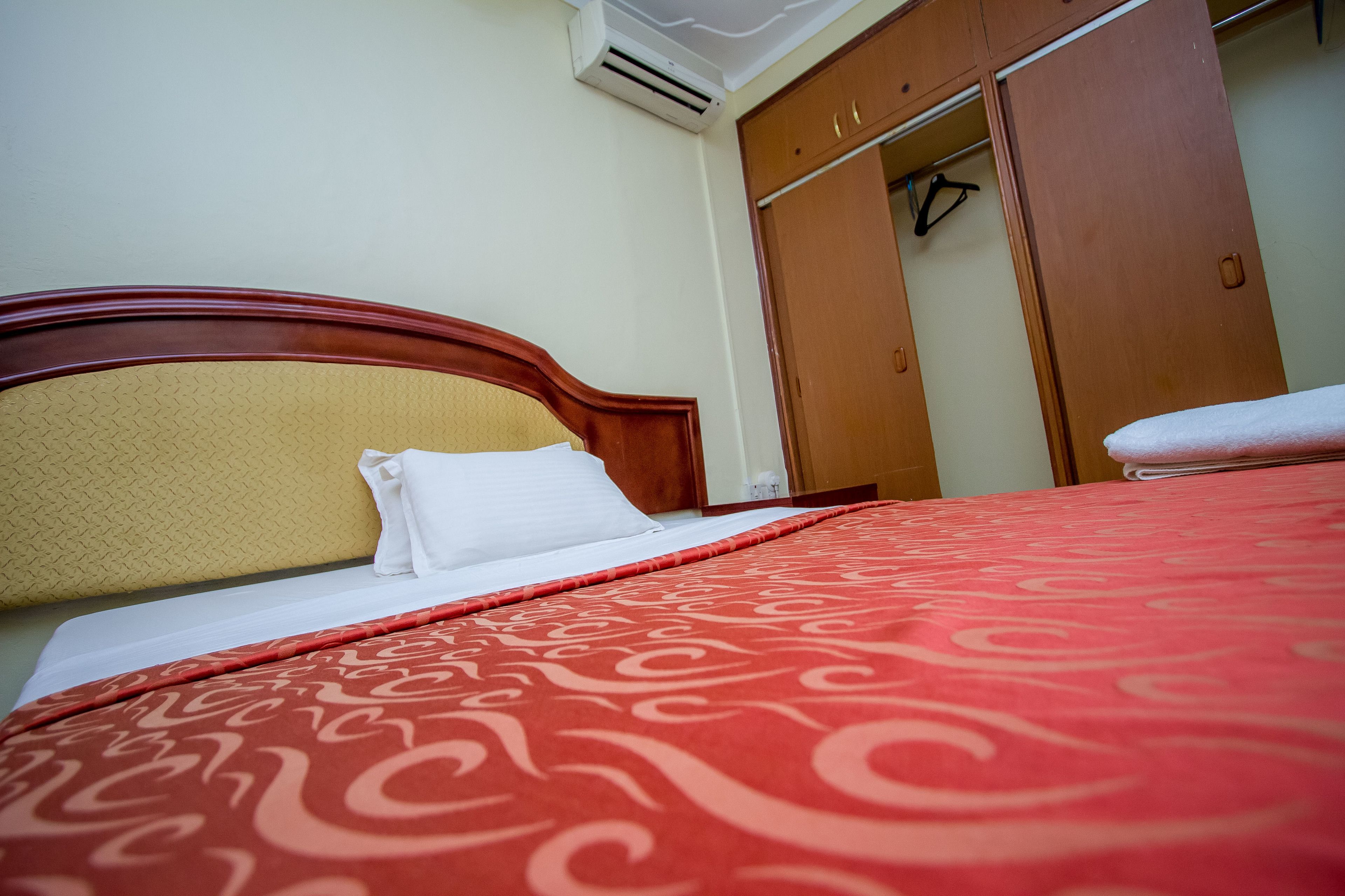 A neatly made bed with a patterned red bedspread, a wooden headboard, and a white pillow.