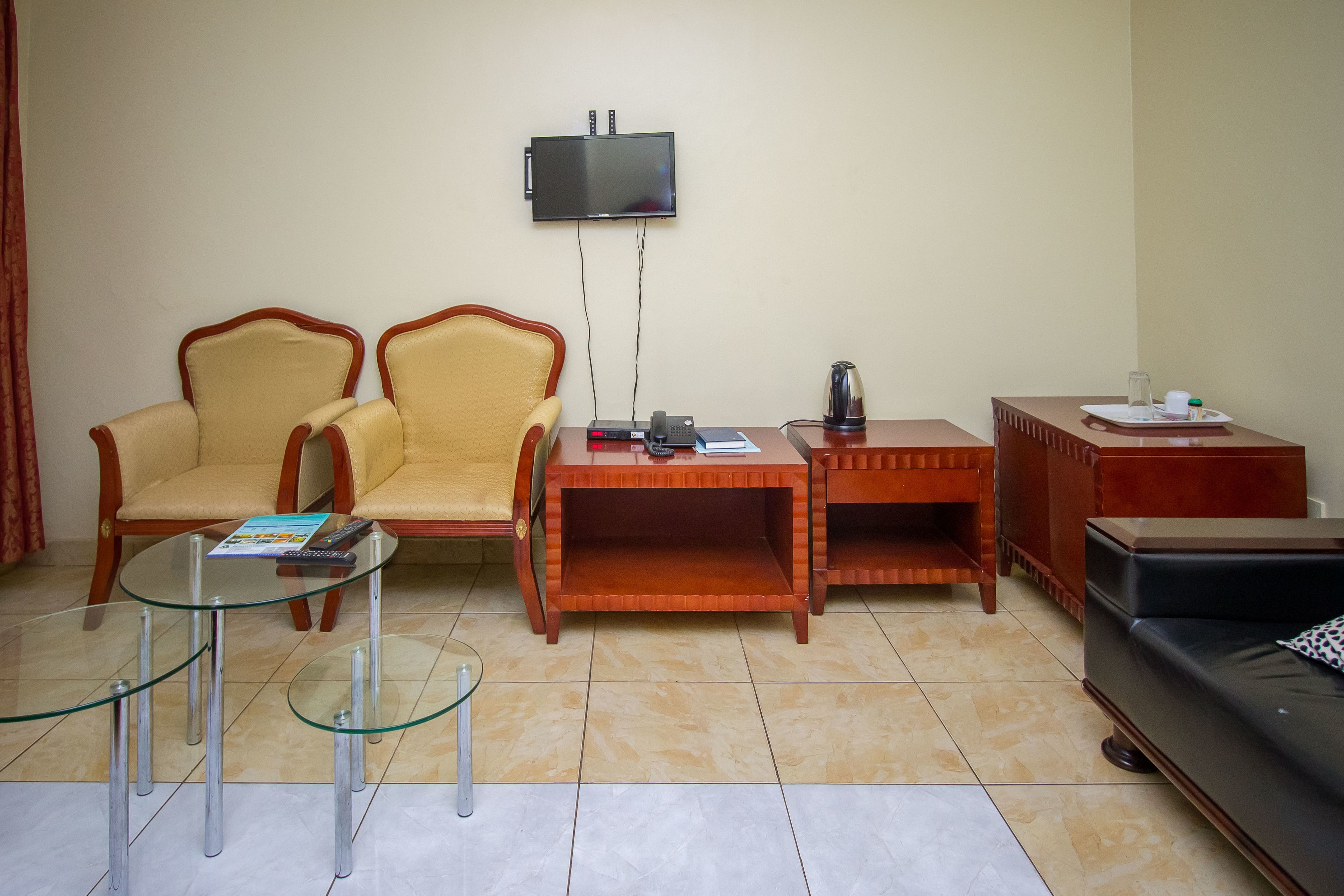 Een woonkamer met een aan de muur bevestigde televisie, twee fauteuils, een salontafel, een bank en een bijzettafeltje met een waterkoker en kopjes.