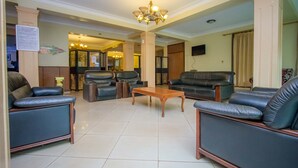 Um hall amplo com sofás de couro, uma mesa de centro de madeira e um lustre.