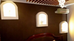 Quarto com cabeceira de madeira, cama com roupa de cama branca e listrada e três luminárias fixadas na parede.
