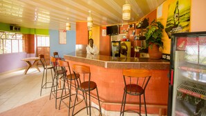 Una zona de bar con mostrador, taburetes, televisor y nevera llena de bebidas.