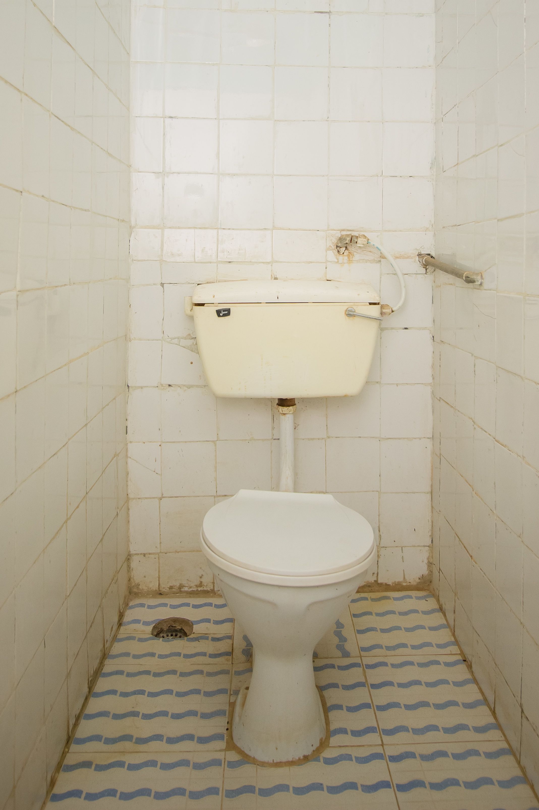 Un baño pequeño y estrecho, con inodoro blanco, paredes y suelo de azulejos.