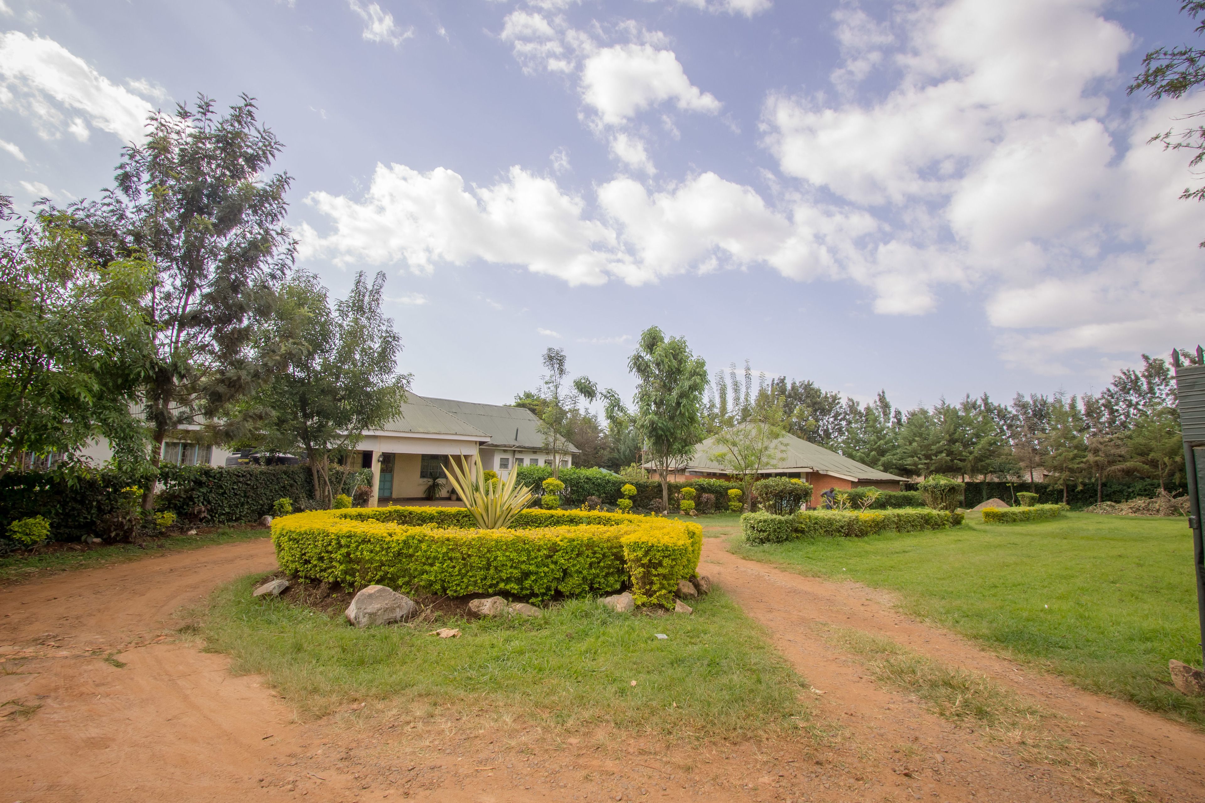 A residential area with a dirt path leading to a house with a covered porch.