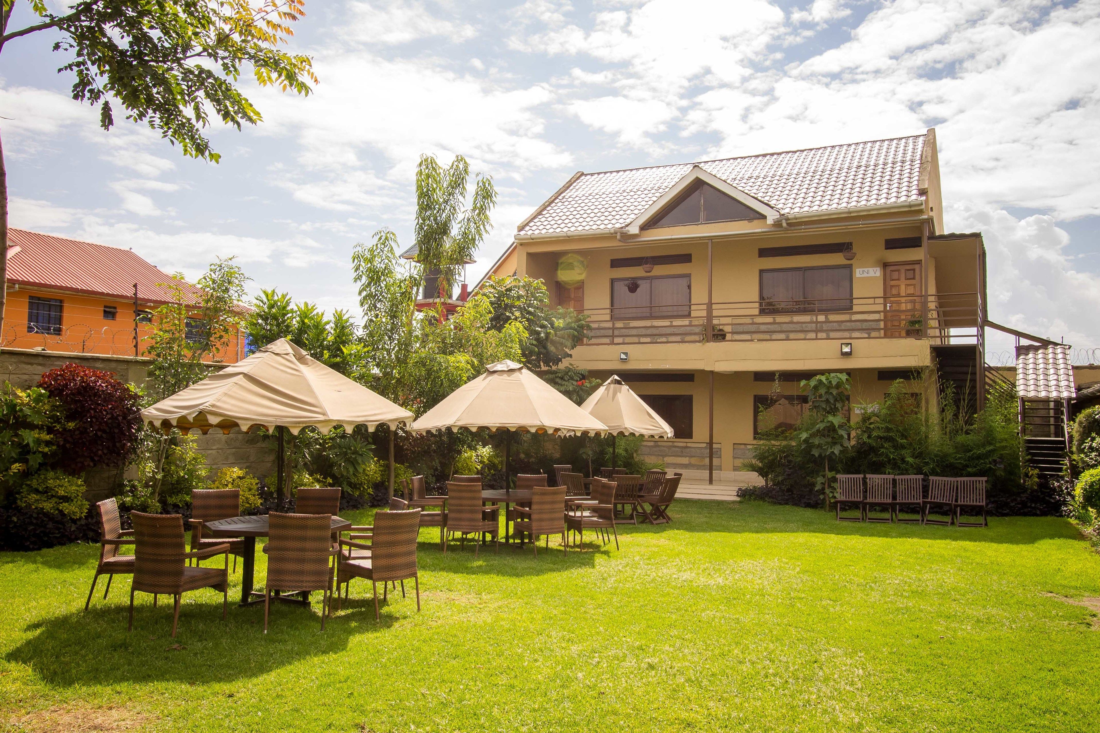 A two-story building with a balcony, surrounded by a well-maintained lawn and outdoor seating area with umbrellas.