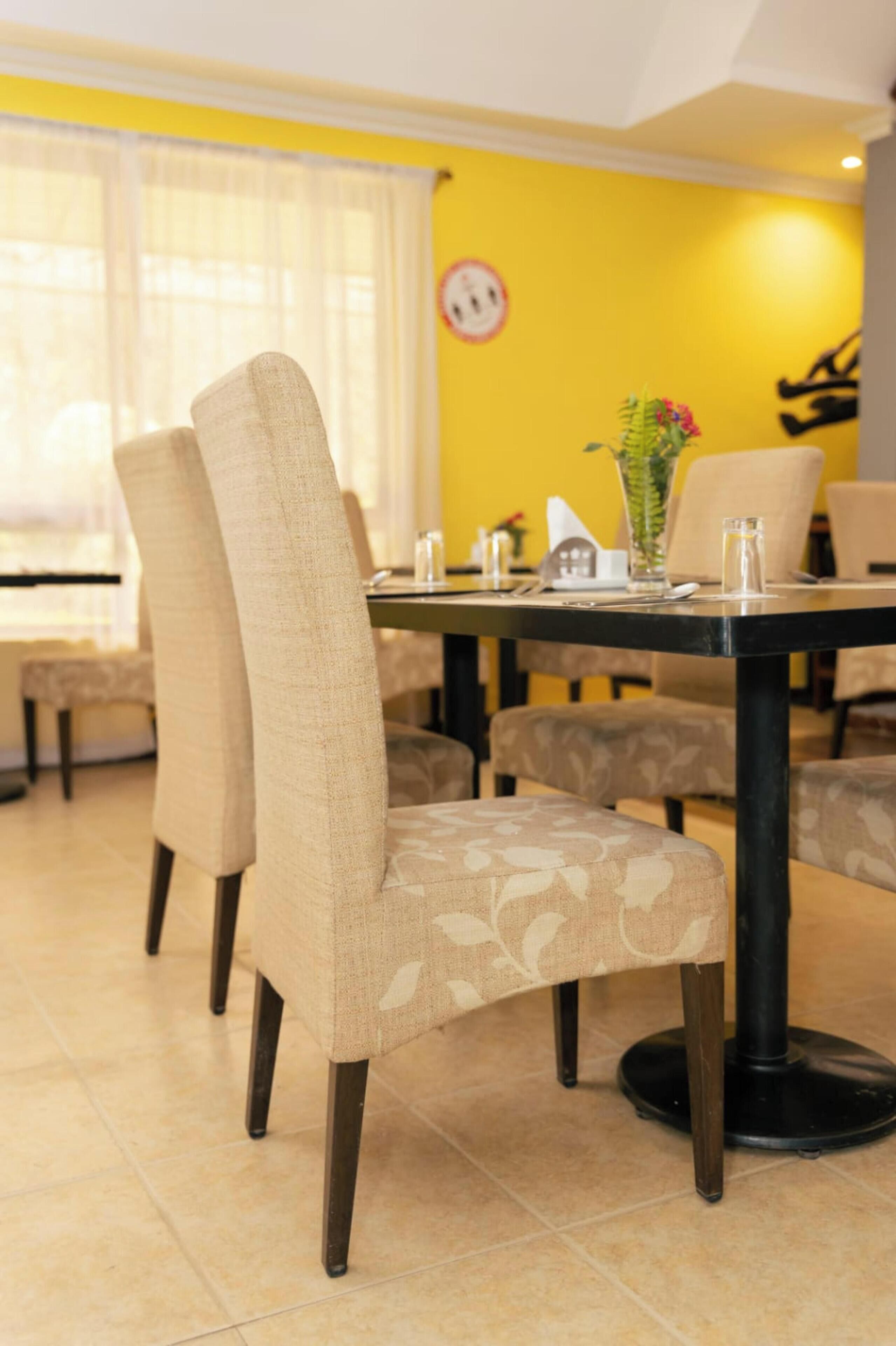 Comedor con pared amarilla, una mesa redonda y sillas tapizadas con un estampado.