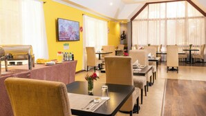 Un comedor de hotel con varias mesas y sillas, una barra de buffet y un televisor montado en la pared.