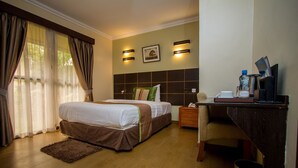 Habitación de hotel bien iluminada con una cama grande, un escritorio con silla y un pequeño cubo de basura.