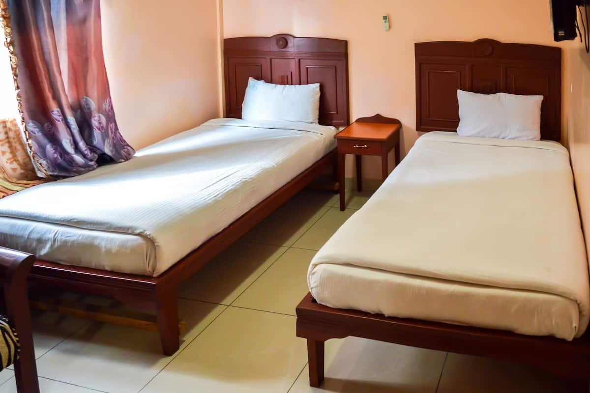 A hotel room with two single beds, a wooden headboard, a small bedside table, and a curtain with a floral pattern.