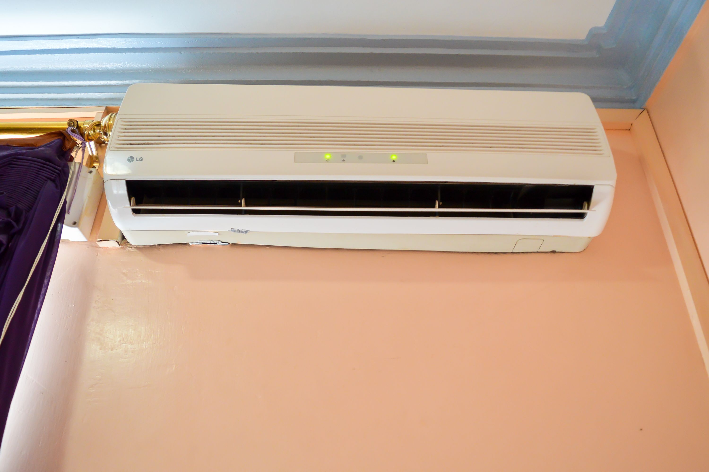 An LG air conditioner unit mounted on a wall with a control panel displaying three indicator lights.