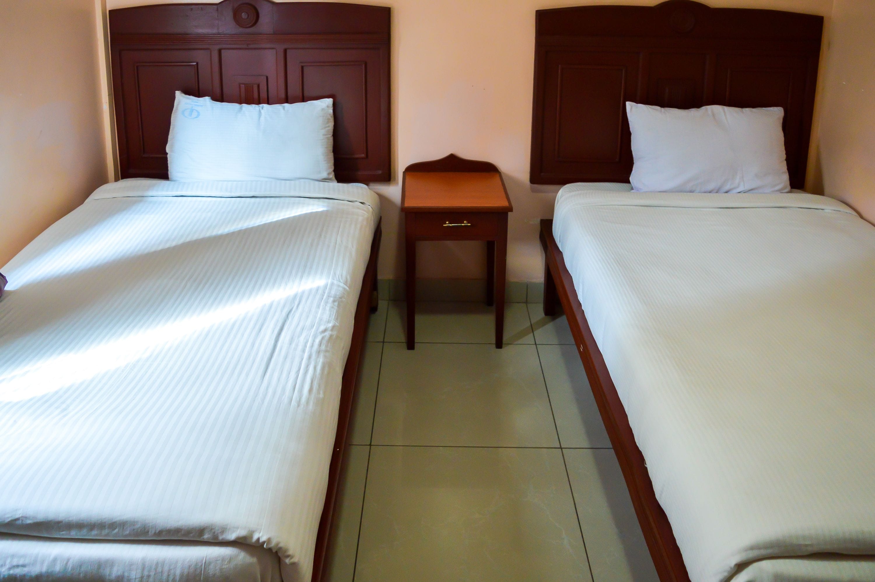 A hotel room with two single beds, each with a wooden headboard and white bedding.
