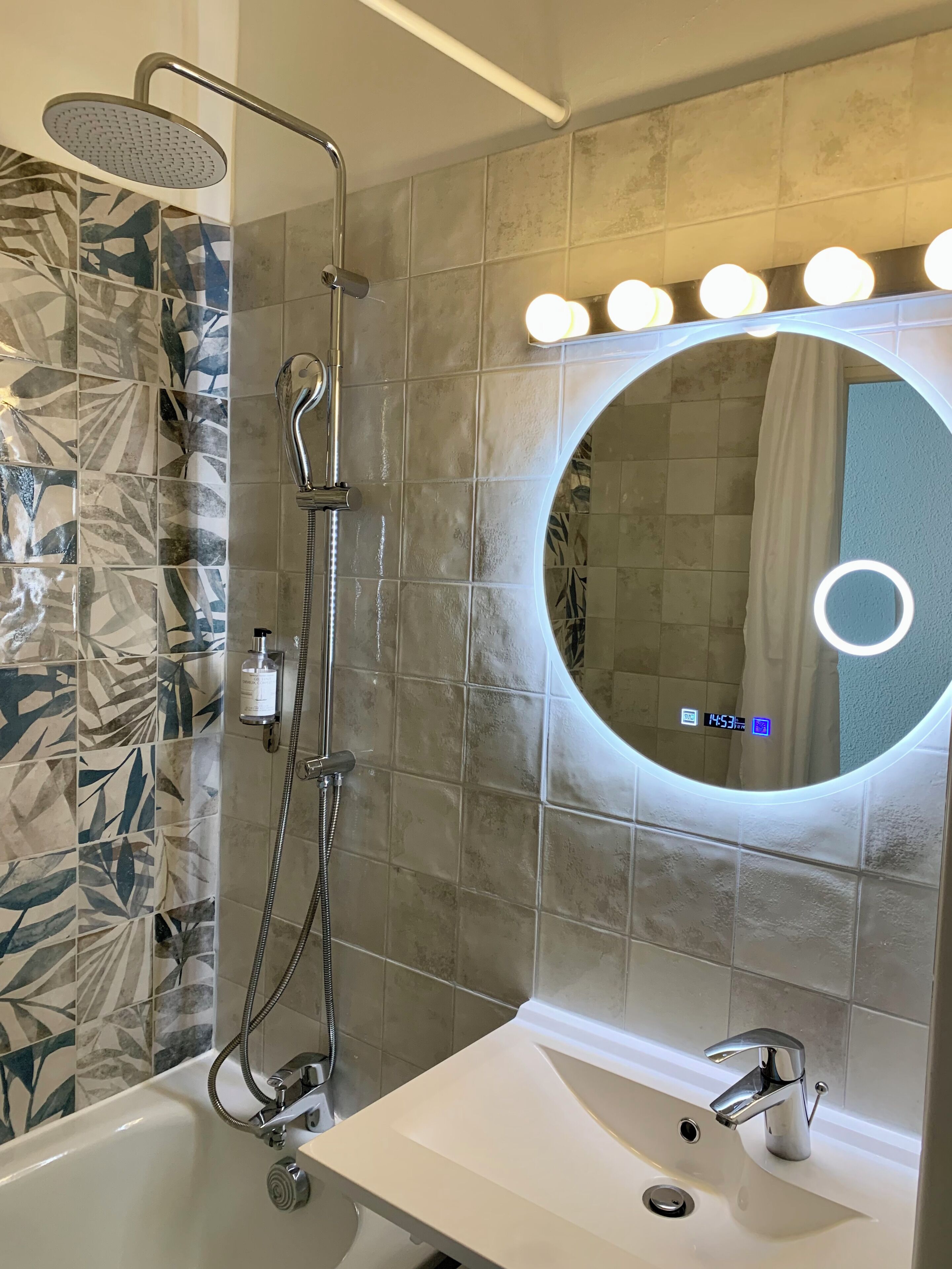 A bathroom with a shower, a sink, and a mirror with lights.