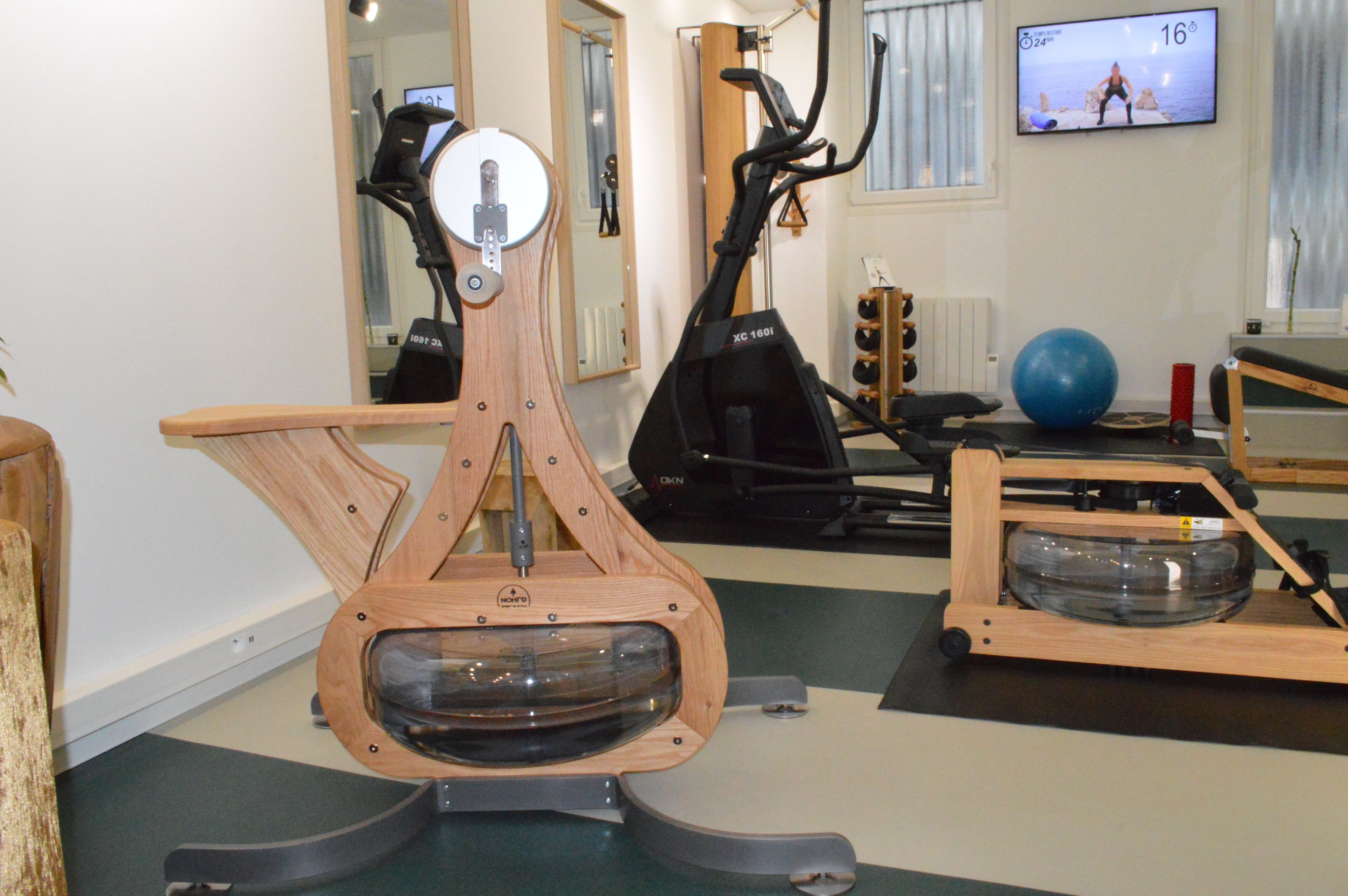A home gym with a wooden rowing machine, an elliptical trainer, and a blue exercise ball.