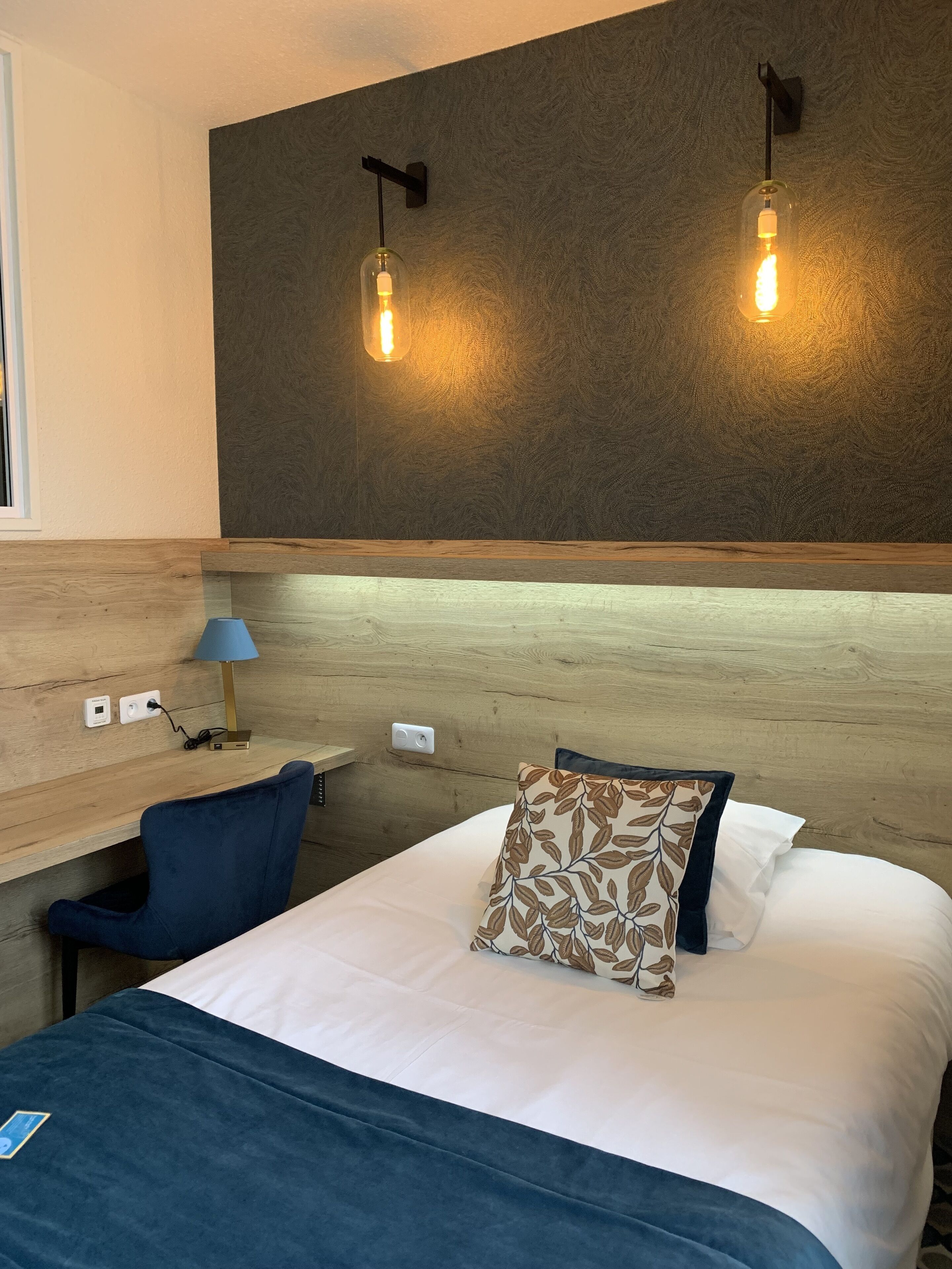 A hotel room with a bed, a desk, a chair, and two wall-mounted lights.