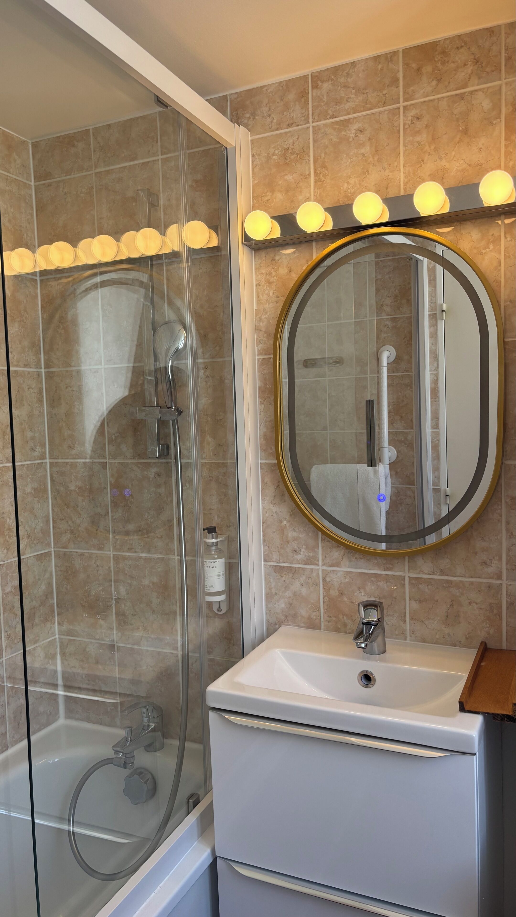 Une salle de bain avec une douche à parois de verre, un lavabo avec un miroir au-dessus et un meuble-lavabo doté d’un porte-serviettes.