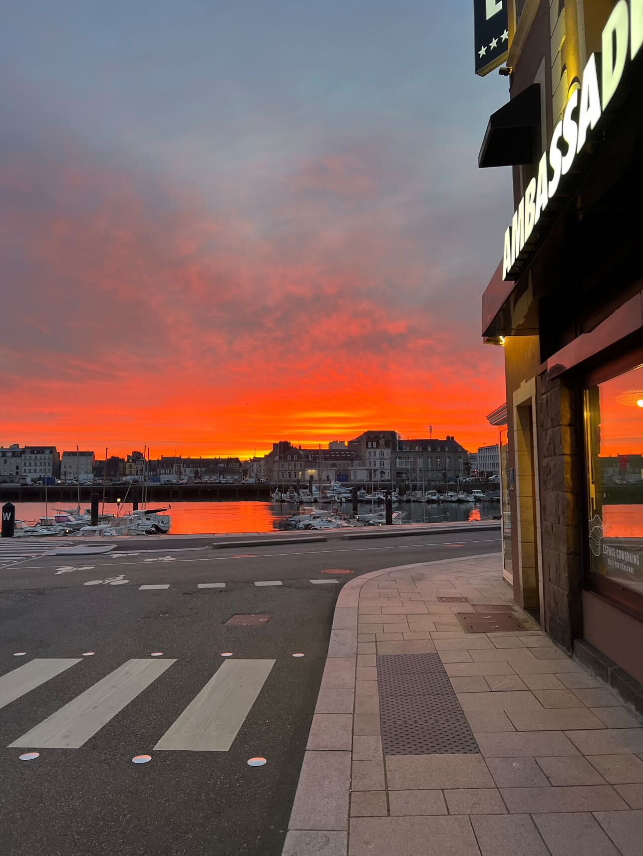 Vista al frente del agua con un atardecer, un paso de peatones y un edificio con un cartel que dice "THRASSADA".