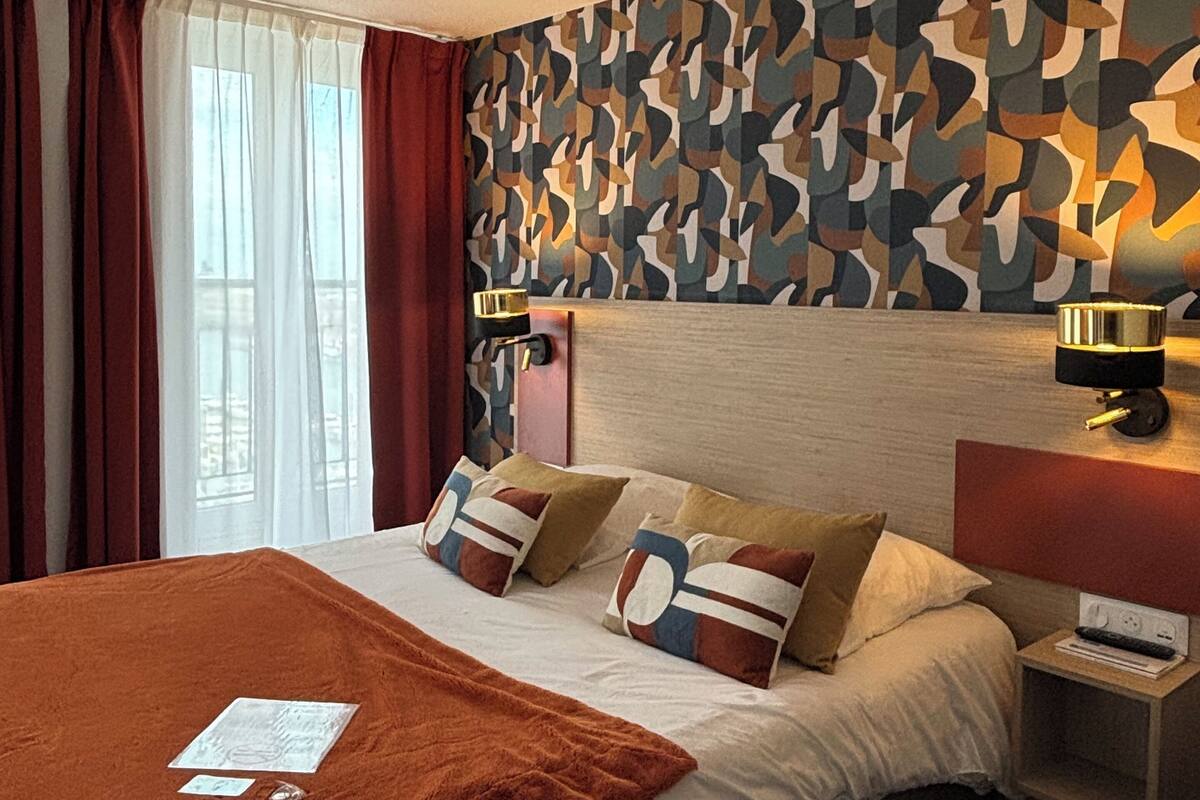 A hotel room with a bed, a nightstand, a wall-mounted lamp, and a patterned wall.