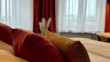 Ein Bett mit roten und gelben Kissen, ein weißer Kopfteil und ein Fenster mit transparenten Vorhängen.