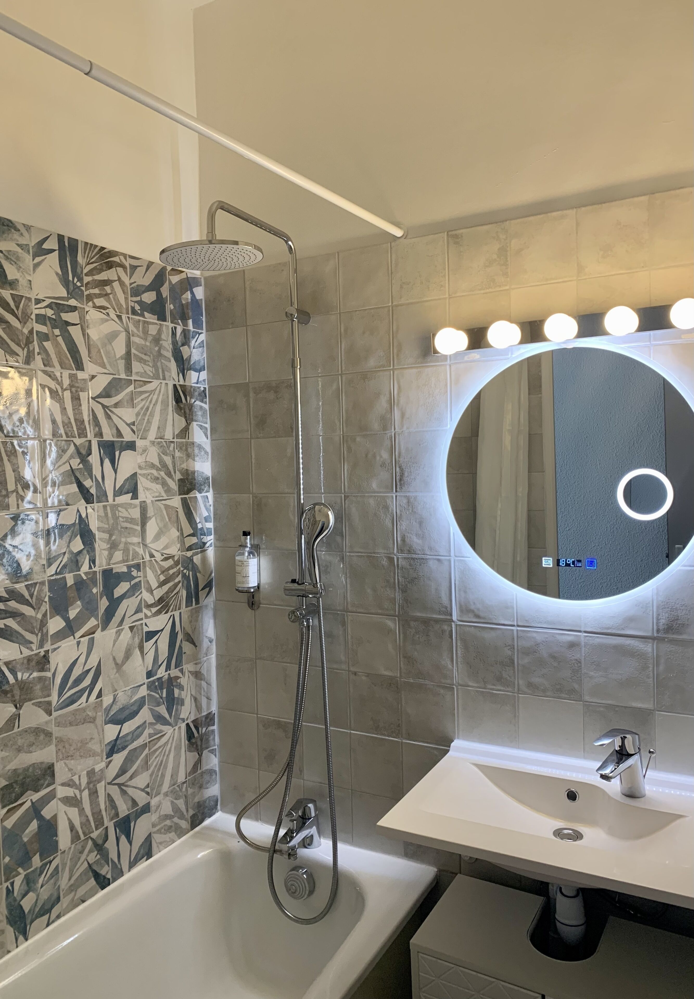 A bathroom with a shower, a sink, and a mirror with lights.
