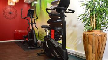 Un gimnasio con equipo de ejercicio, una gran jardinera de madera y una pared roja con un diseño geométrico.