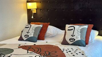 A bed with a patterned bedspread and two decorative pillows, a wall-mounted lamp, and a tufted headboard.