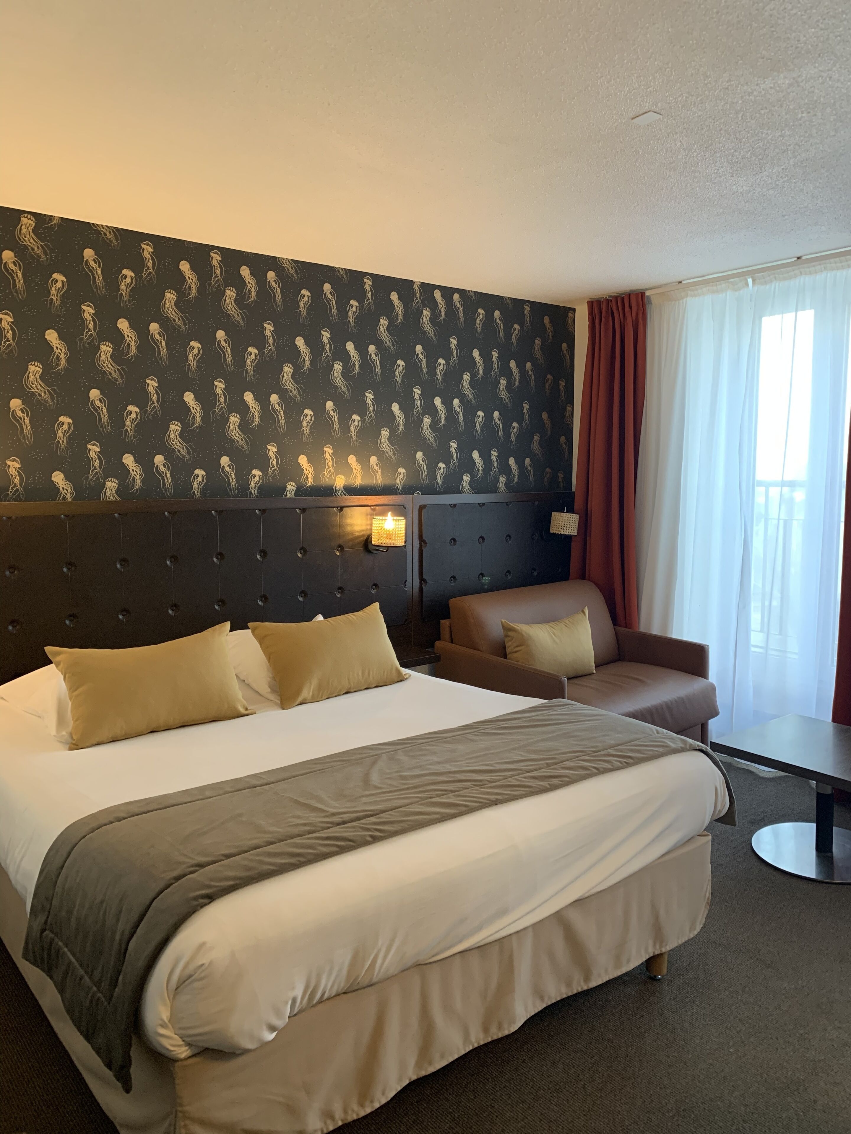 Una habitación de hotel con una cama grande, un sofá, una mesita y una pared con un diseño.